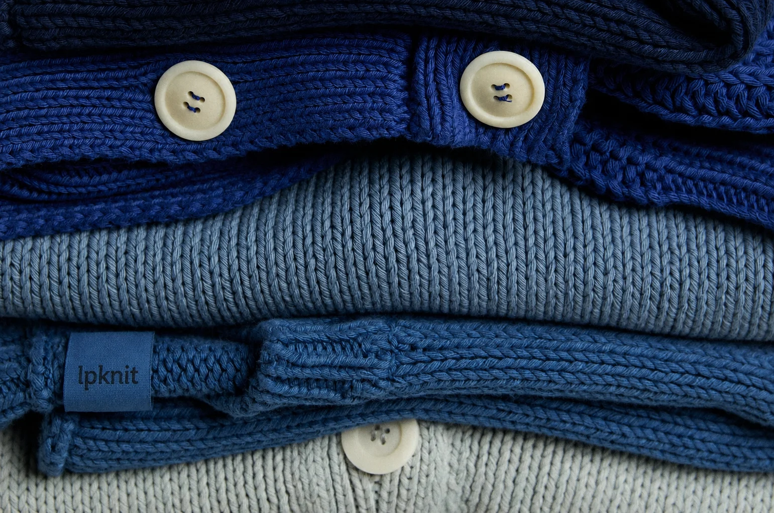 Stack of folded lpknit knit sweaters showing the brand label and natural buttons