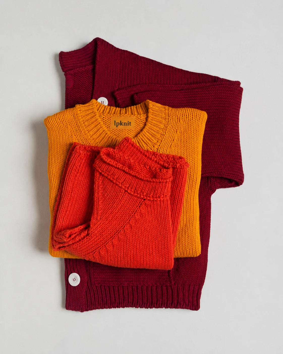 Folded burgundy, mustard and red lpknit sweaters with the woven lpknit label